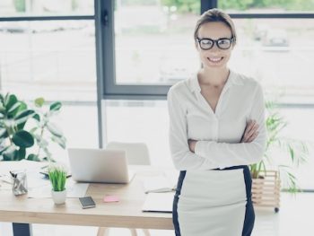 Pretty Business Woman Is Standng With Crossed Hands Near Her Desk In Light Modern Work Place, Smiling And Looking At Camera. Development, Leadership, Authority, Feminity Concept